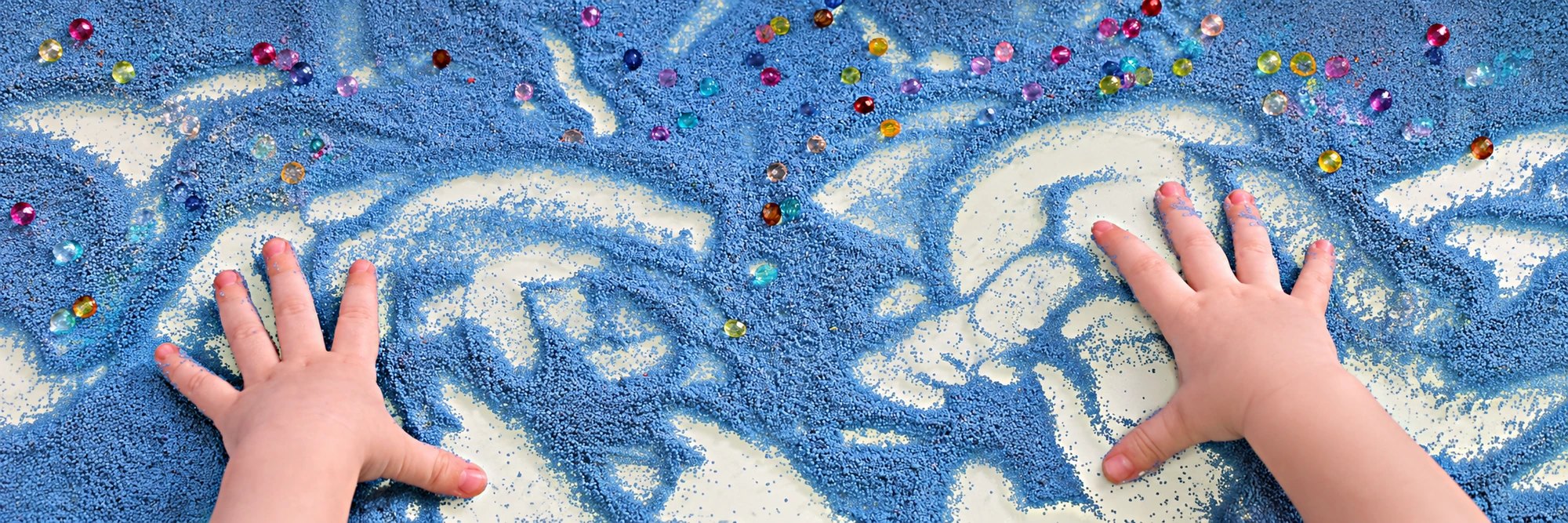 Children's hands drawing in green sensory sand